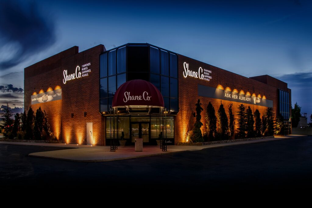 The exterior of Shane Co. building illuminated by strategically placed landscape lighting, highlighting the brick façade and surrounding greenery.