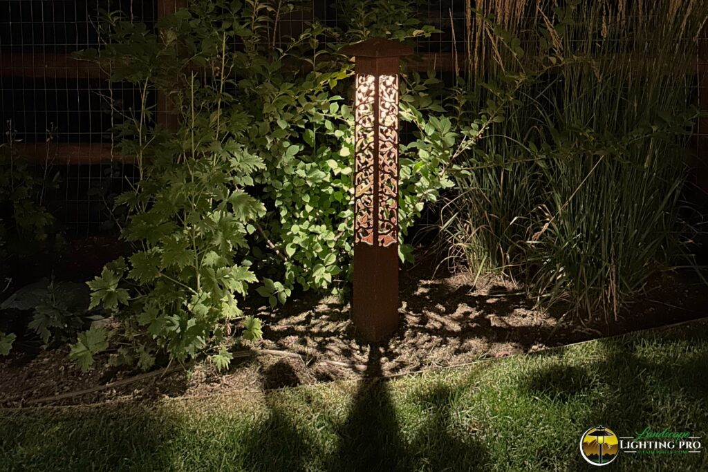 bollard light in garden bed, casting a shadow of the fixture