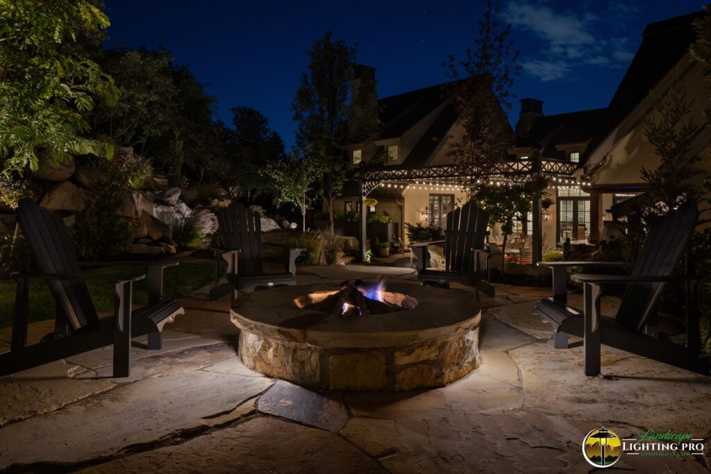 Outdoor fireplace highlighted by undercap lighting, with a pergola in the background draped in bistro lights