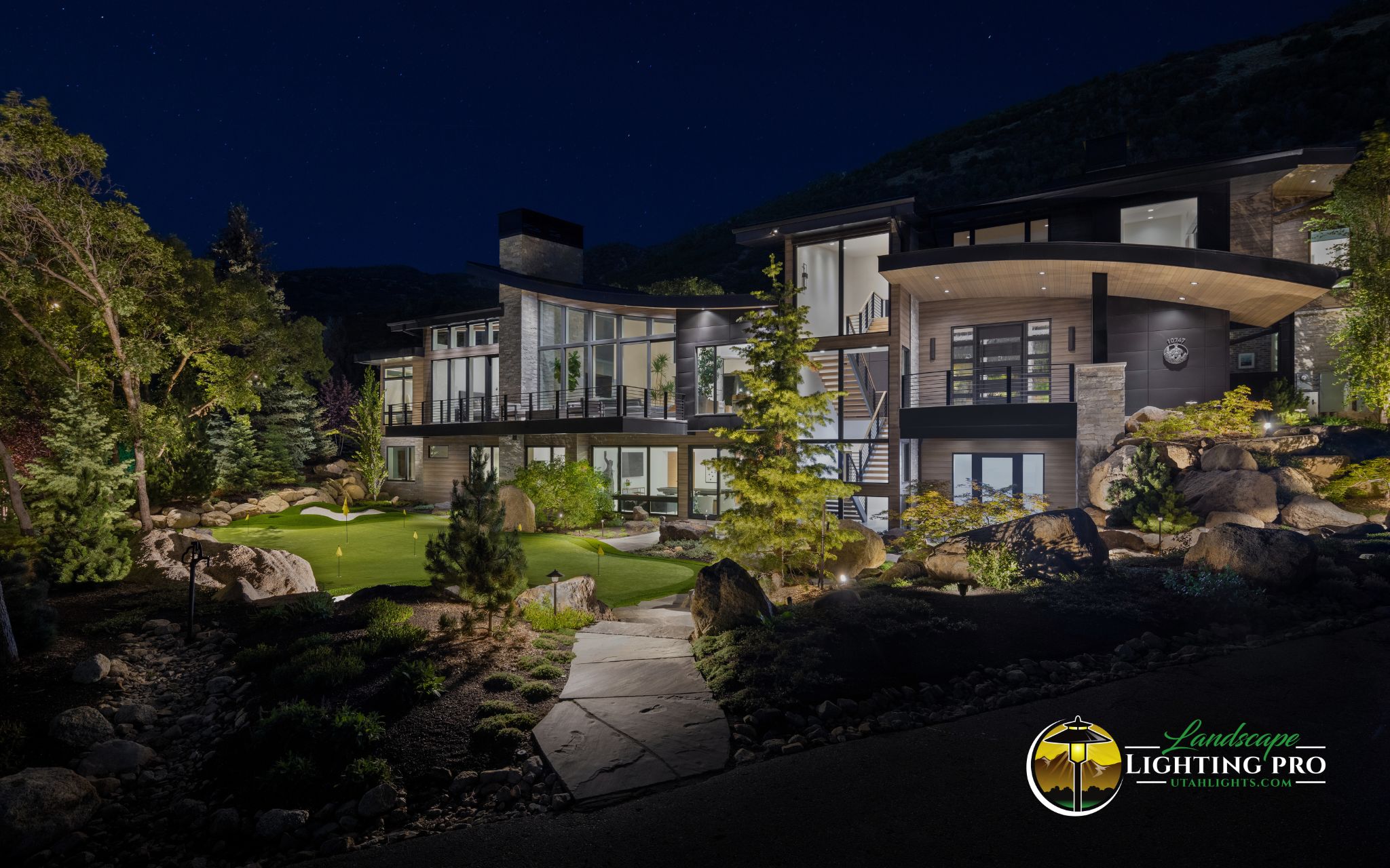 Modern luxury home with custom landscape lighting showcasing warm uplighting on trees, boulders, and architectural textures — designed to enhance curb appeal after dark