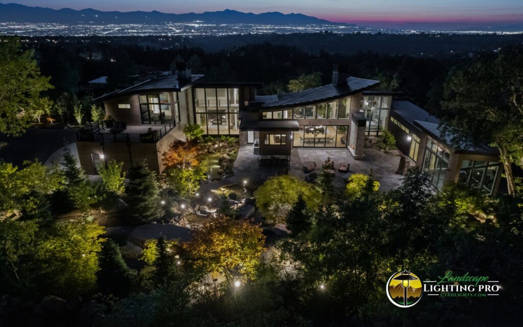 Twilight view of a luxury hillside home with elegant landscape lighting illuminating trees, gardens, and architectural elements — blending natural beauty with high-end lighting design.