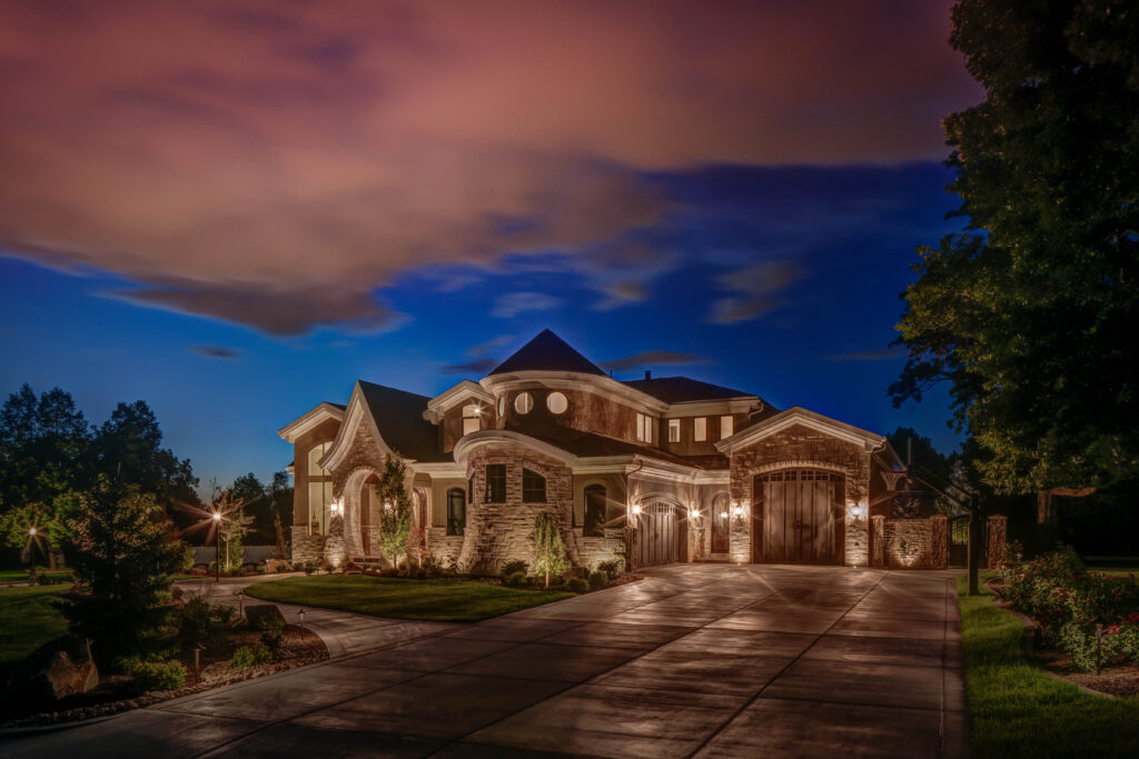 Elegant stone luxury home at twilight with soft architectural lighting highlighting the facade, entryway, and driveway — showcasing refined outdoor lighting design.